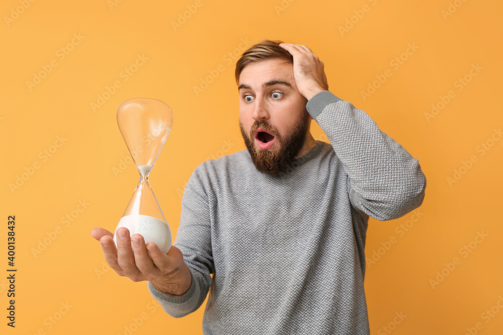 Shocked young man with hourglass on color background Shocked young man with hourglass on color background