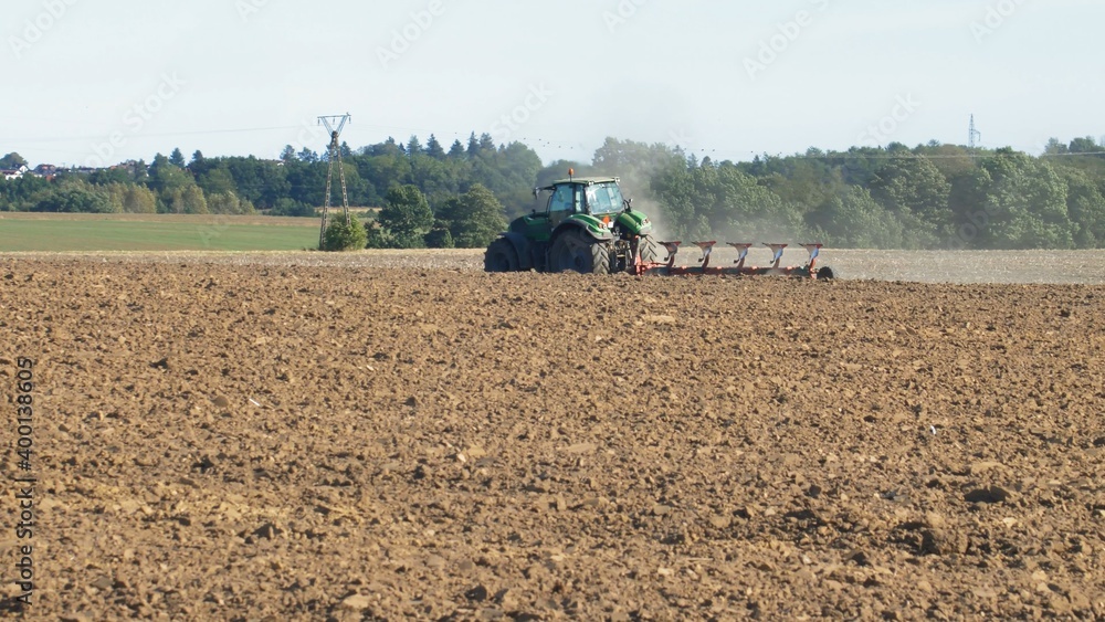 Fototapeta premium Farmer Ploughing Soil using Tractor with Mouldboard Plough on Sunny Day