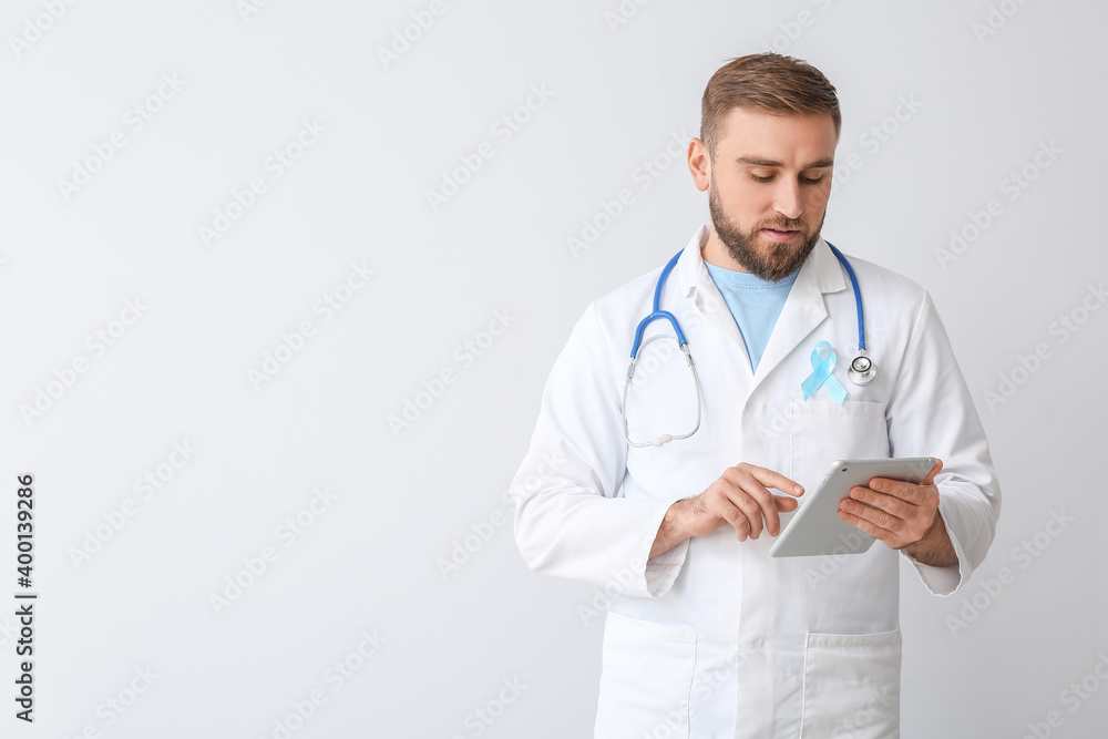 Doctor with blue ribbon and tablet computer on light background. Prostate cancer awareness concept