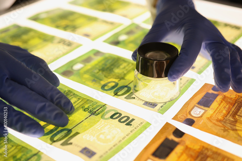 Hands in rubber gloves holding magnifying glass over banknotes closeup photo