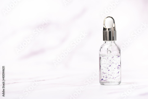 A bottle of cosmetic oil for skin care on a light marble background. Falling drop of oil from a pipette close-up. Beneficial enzymes and vitamins of squalene, flower water and beauty serum. photo