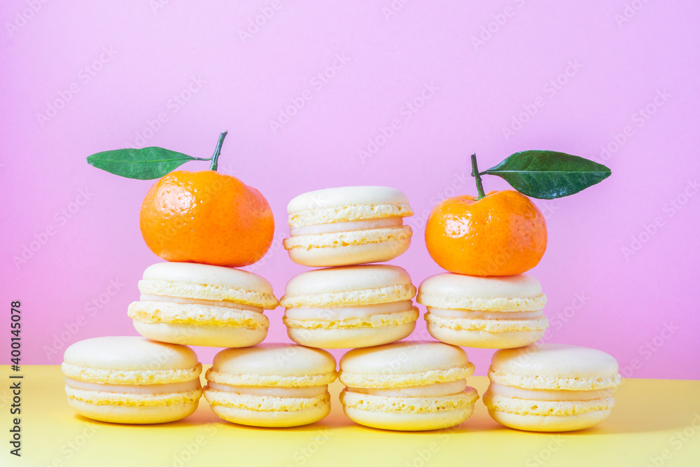 Pyramid of yellow French macaroon pastries with lemon cream on a yellow and pink background with orange tangerine. Valentine's day gift Pyramid of yellow French macaroon pastries with lemon cream on a yellow and pink background with orange tangerine. Valentine's day gift