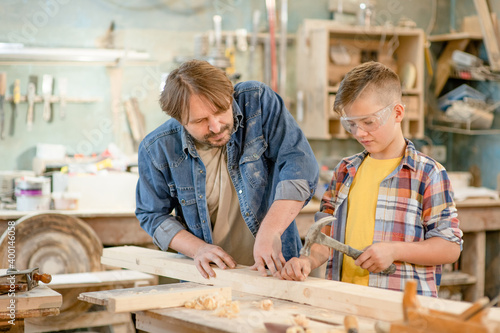 Father teaches son to hammer nails in the workshop. Empty space for text