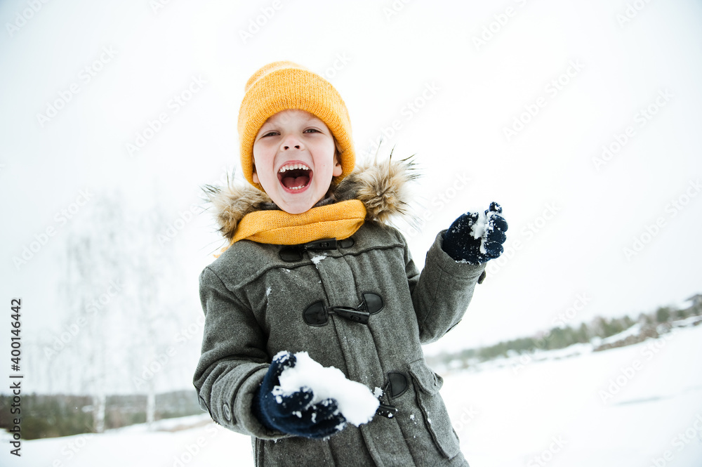 Fototapeta premium Cute a boy in warm yellow hat and gray overcoat walking in winter the forest.