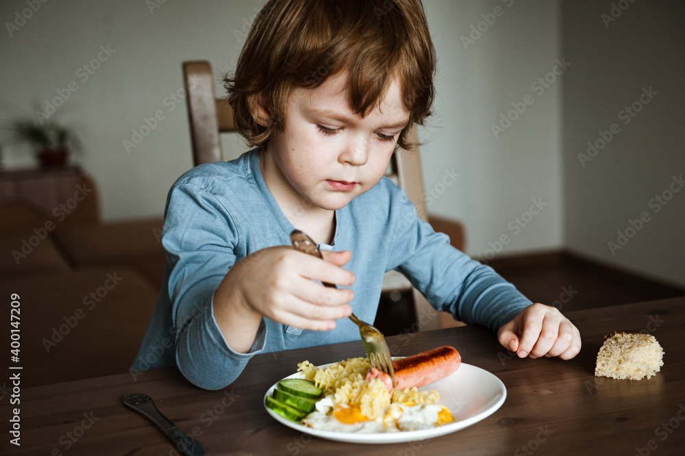 Cute preschooler boy has lunch at home.