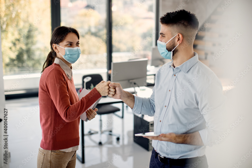 Happy entrepreneurs fist bumping while greeting in the office during COVID-19 pandemic. Happy entrepreneurs fist bumping while greeting in the office during COVID-19 pandemic.