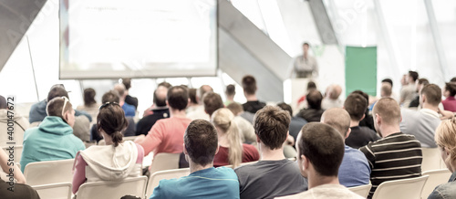 Man giving presentation in lecture hall. Male speeker having talk at public event. Participants listening to lecture. Rear view, focus on people in audience.