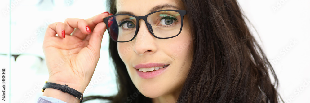Portrait of smiling woman in glasses on background of showcase with optics. How to choose the right eyeglass frame concept Portrait of smiling woman in glasses on background of showcase with optics. How to choose the right eyeglass frame concept