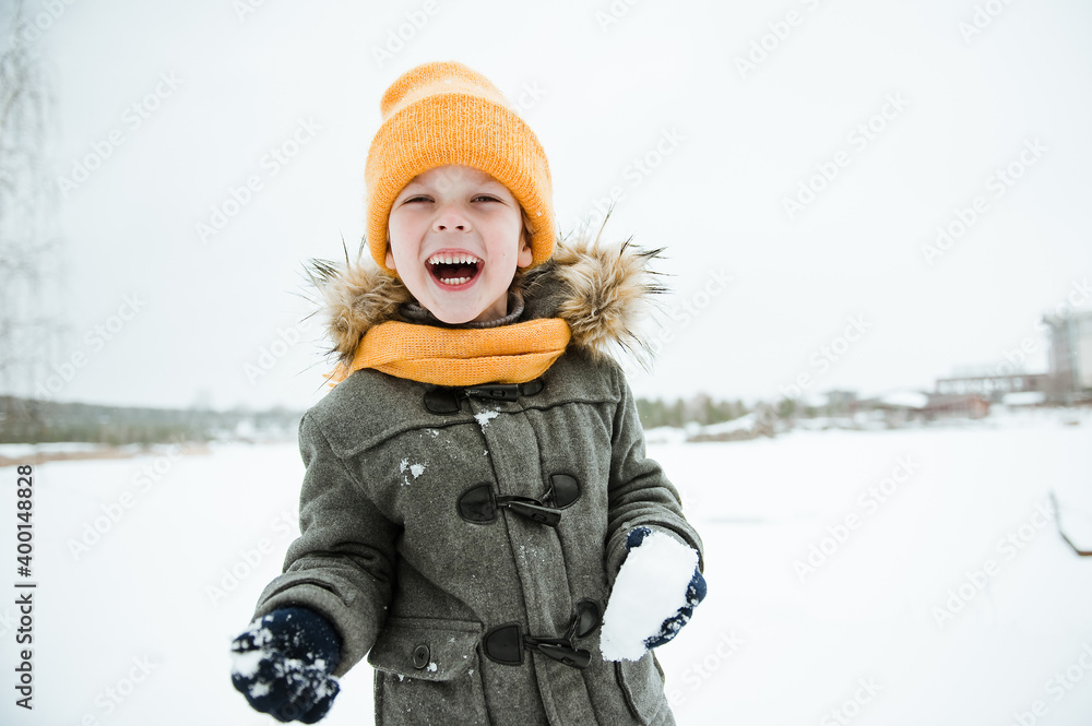 Cute a boy in warm yellow hat and gray overcoat walking in winter the forest. Cute a boy in warm yellow hat and gray overcoat walking in winter the forest.