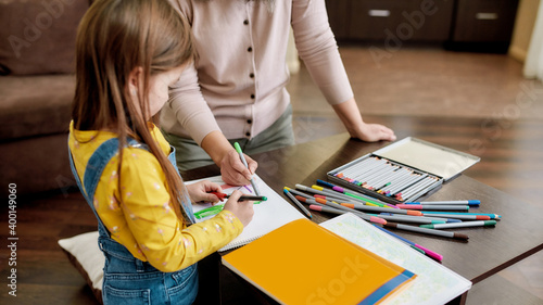 Little girl drawing in album using felt pens with babysitter
