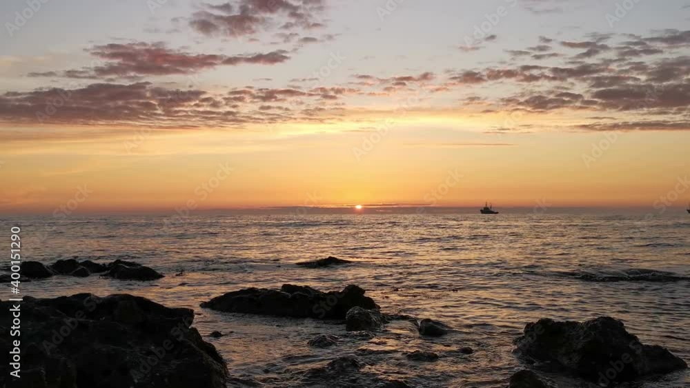 Beautiful orange sunset over the sea. The calm movement of the waves breaking and the stone shore. A small silhouette of a ship on the horizon.The concept of relaxation and privacy. The seaside resort Beautiful orange sunset over the sea. The calm movement of the waves breaking and the stone shore. A small silhouette of a ship on the horizon.The concept of relaxation and privacy. The seaside resort