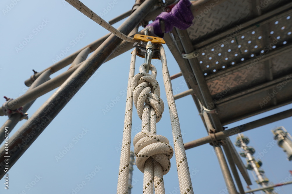 White rope with figure of eight knot into Aluminum safety harness loop equipment and pulley to rescue workers in case of incident at industrial construction project.