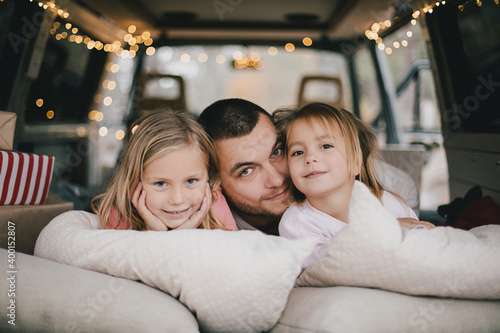 Happy father and his kids having fun in a van decorated with festive Christmas lights. © polinaloves
