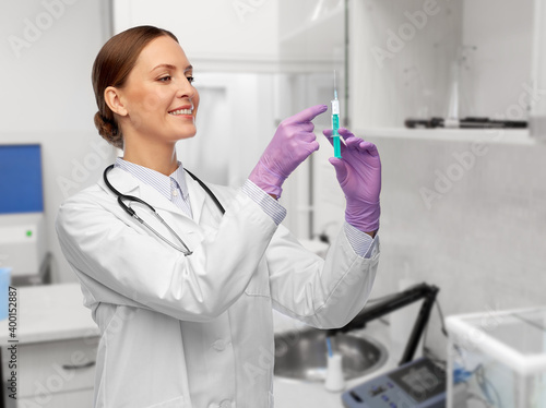 medicine, vaccination and healthcare concept - happy smiling female doctor with stethoscope and syringe over hospital background