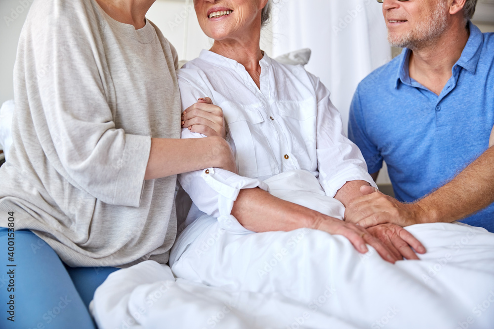 Obraz premium medicine, support, family health care and people concept - happy senior man and young woman visiting and cheering her grandmother lying in bed at hospital ward