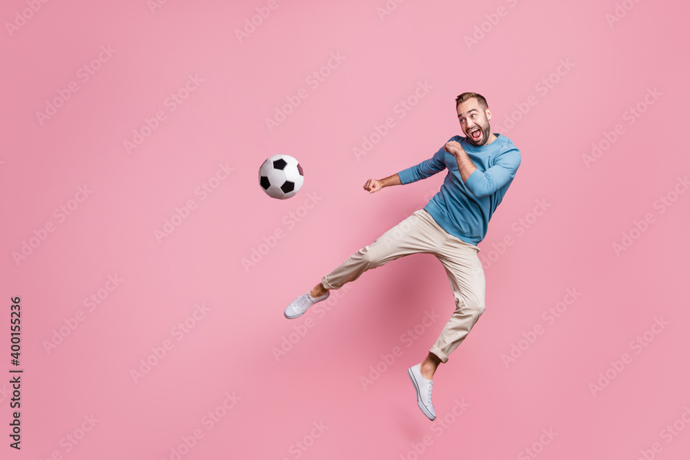 Full length photo of sweet strong young man dressed blue sweater jumping high kick foot ball isolated pink color background