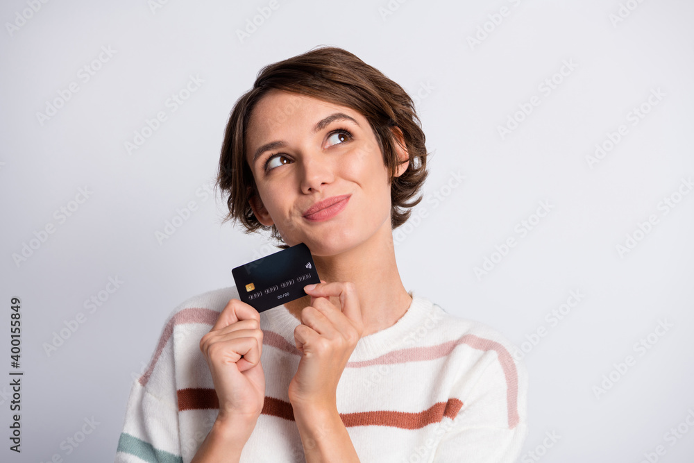 Photo of thoughtful young lady wear striped sweater holding bank card looking empty space isolated grey color background Photo of thoughtful young lady wear striped sweater holding bank card looking empty space isolated grey color background