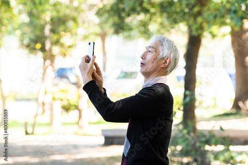 スマートフォンで公園の自然を撮影するおじいちゃん