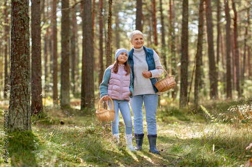 picking season, leisure and people concept - grandmother and granddaughter with baskets and mushrooms in forest © Syda Productions