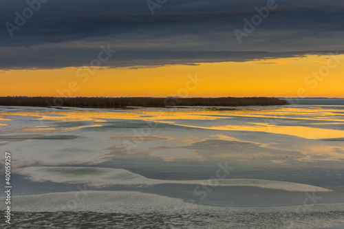 frozen lake with reed during sunset with rain clouds