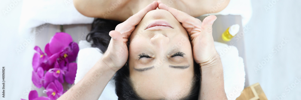 Woman lies on massage table with her eyes closed, masseur holds her hands on the lines of the chin. Facial care and effective facial massage concept Woman lies on massage table with her eyes closed, masseur holds her hands on the lines of the chin. Facial care and effective facial massage concept