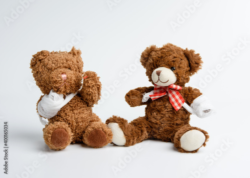 brown curly teddy bear with rewound paw with white gauze bandage on white background