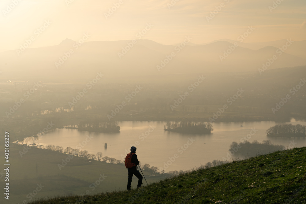 Male hiker looking at rolling landscape and hills of Czech Central Mountains at sunset