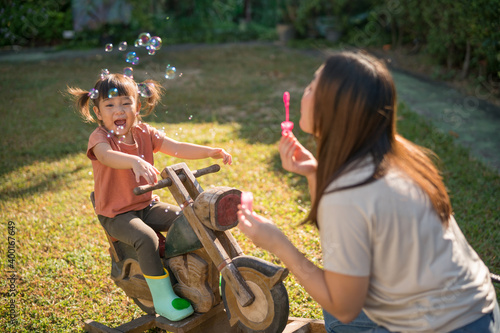 Selective focus, Happy family concept, Mother and lovely daughter blowing soap bubbles in the garden. little girl on the wooden rocking horse.
