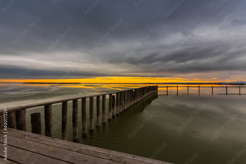 long wooden railing on a frozen lake with rain clouds and sun on the horizon