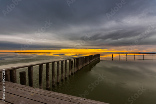 long wooden railing on a frozen lake with rain clouds and sun on the horizon