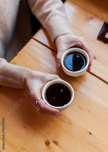 woman holds in hands two ceramic mug with black coffee. alternative brewing method of specialty coffee. background light wood. coffee shop interior