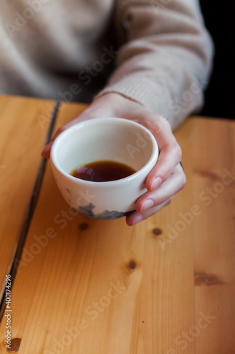 Young woman holds in hand ceramic white cup with black coffee or tea. alternative brewing of specialty coffee. light beige wood table background