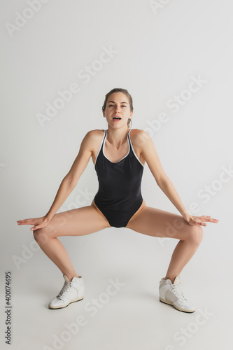 Magazine. Beautiful young woman's isolated on grey studio background. Having fun, happy, full length. Dancing, getting crazy mood, having fun. Stylish girl in black sportive swimsuit. Copyspace.