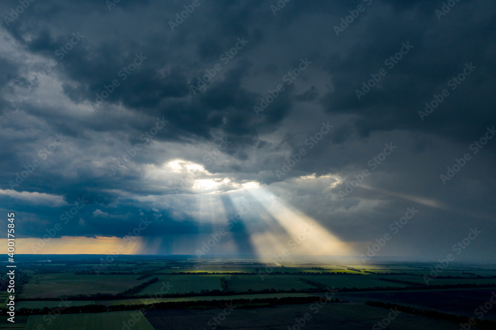 Aerial flying above stunning field under dramatic rain cloud rolling. Global warming effect black thunderstorm dramatic rain clouds Dramatic sky. Light rays shining through clouds