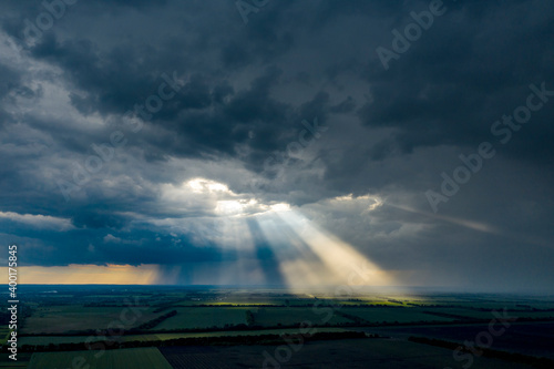 Aerial flying above stunning field under dramatic rain cloud rolling. Global warming effect black thunderstorm dramatic rain clouds Dramatic sky. Light rays shining through clouds