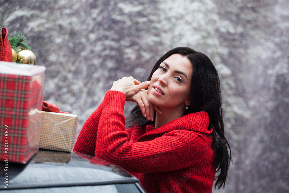 Portrait of happy woman in a red sweater stands at a red car with new year decoration and gifts in a snowy forest. Portrait of happy woman in a red sweater stands at a red car with new year decoration and gifts in a snowy forest.