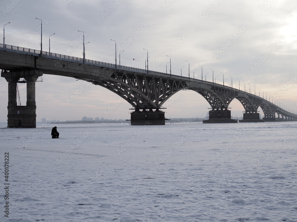 Obraz premium Winter fishing on the ice. The Volga river in Saratov, Russia. Road bridge on the horizon