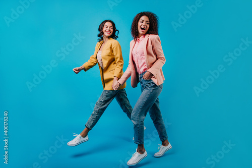 Two well-dressed young ladies posing in studio. Indoor full-length portrait of mixed race women.