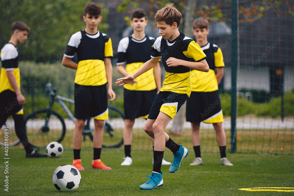 Fototapeta premium Group of teenage boys on football training. Young soccer players kicking ball on practice. School age boys improving sports skills on school training grass pitch