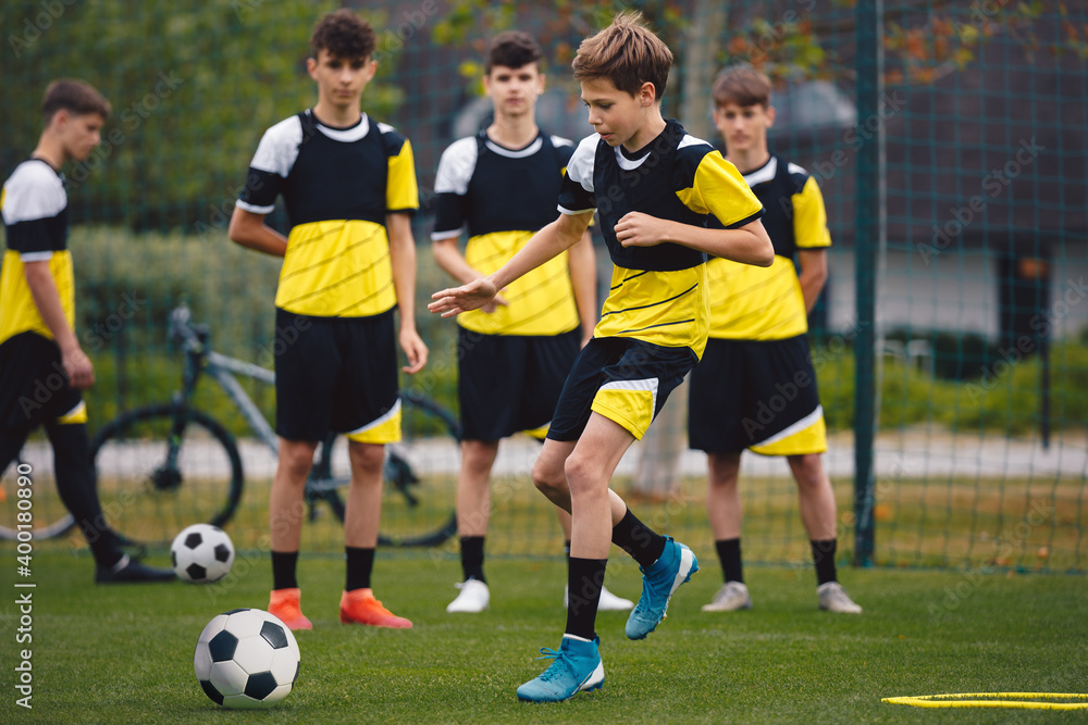 Group of teenage boys on football training. Young soccer players kicking ball on practice. School age boys improving sports skills on school training grass pitch