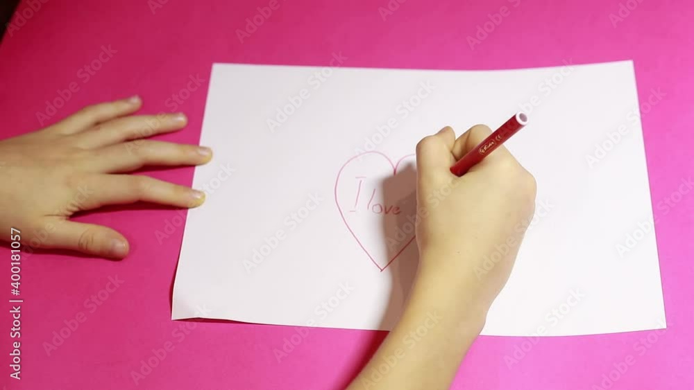 Child hands draw heart on white sheet of paper. Kid write I love you. Video greeting card concept Child hands draw heart on white sheet of paper. Kid write I love you. Video greeting card concept