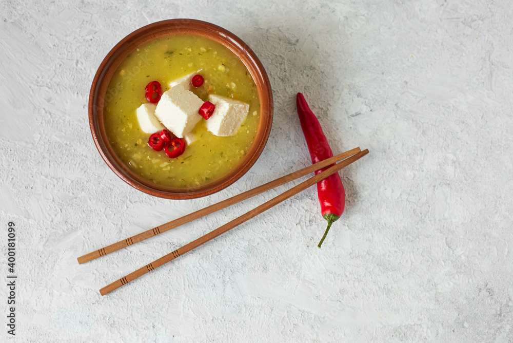 horizontal top view of japanese or asian spicy miso soup with tofu and red pepper in a brown bowl on light background with chopsticks  with copy space