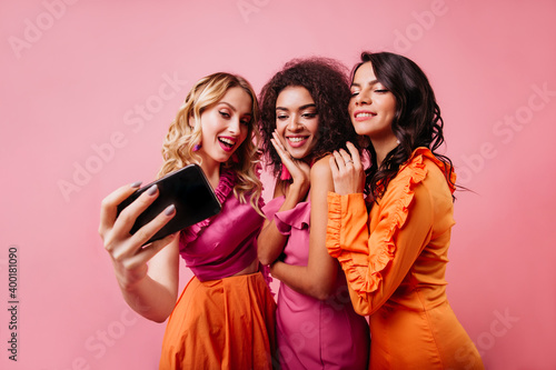 Romantic blonde girl making selfie with friends. Pretty ladies posing on pink background.