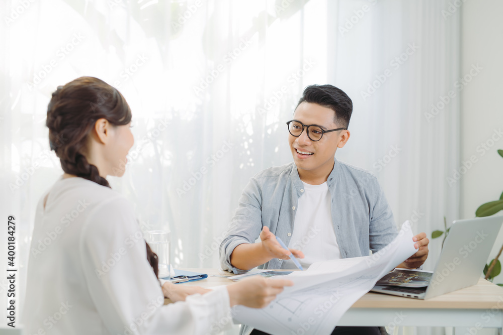 Real-estate agent shows a build project on a digital tablet to young Asian man. Real-estate agent shows a build project on a digital tablet to young Asian man.
