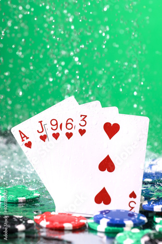 Flush poker combination under the water drops and falling poker chips against green background. Online gambling. Betting. Gambling addiction.