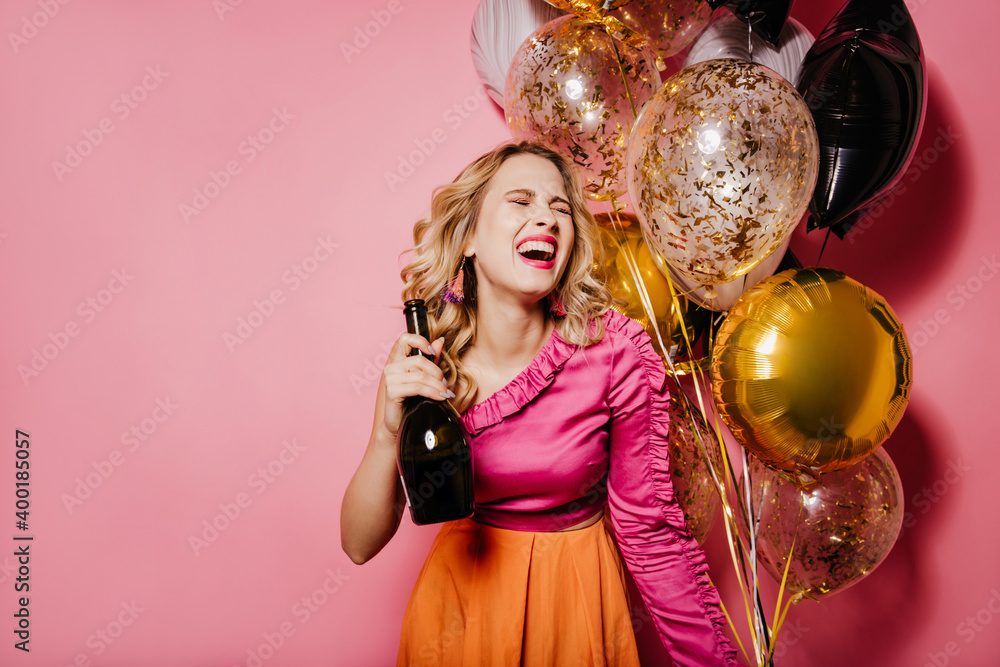 Excited fair-haired woman with champagne laughing on pink background. Studio photo of caucasian female model having fun at party. Excited fair-haired woman with champagne laughing on pink background. Studio photo of caucasian female model having fun at party.