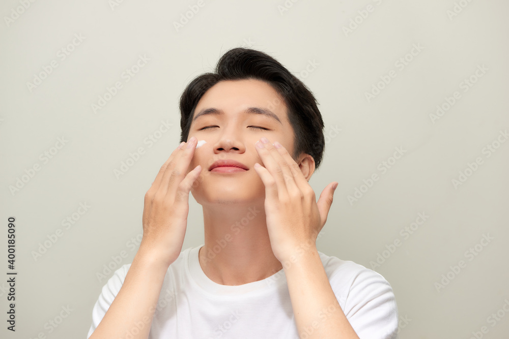 Portrait of satisfied young man applying facial cream isolated over white background Portrait of satisfied young man applying facial cream isolated over white background