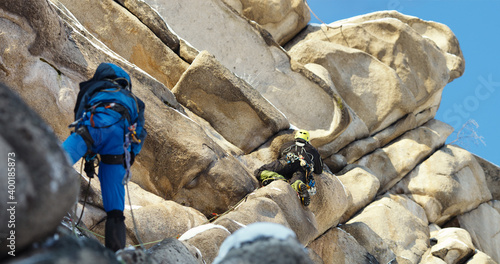 Two mountaineers overcome a difficult rocky wall during a winter ascent in the mountains, panorama.