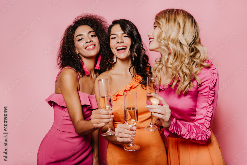 Fashionable girls raising glasses. Studio photo of laughing friends drinking champagne. Fashionable girls raising glasses. Studio photo of laughing friends drinking champagne.