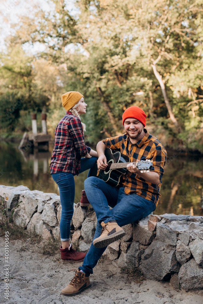a guy in a bright hat plays the guitar with a girl against a background of granite rocks